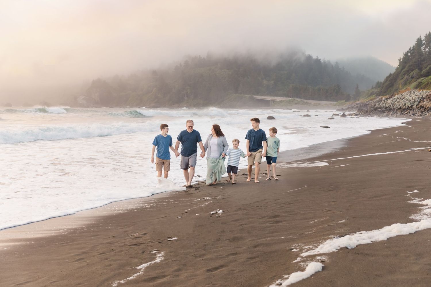 Group walking along a misty beach at sunset with waves crashing on the shore.