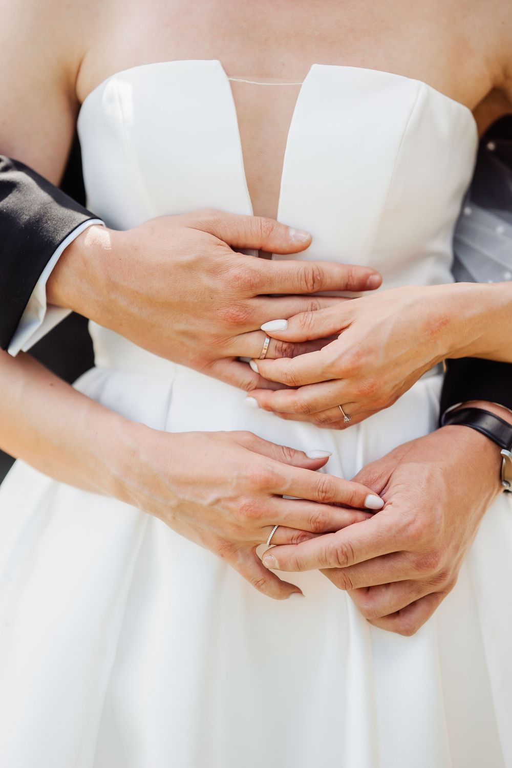 Loving hands embrace around a white wedding dress waist showing wedding rings and tender intimate moment.