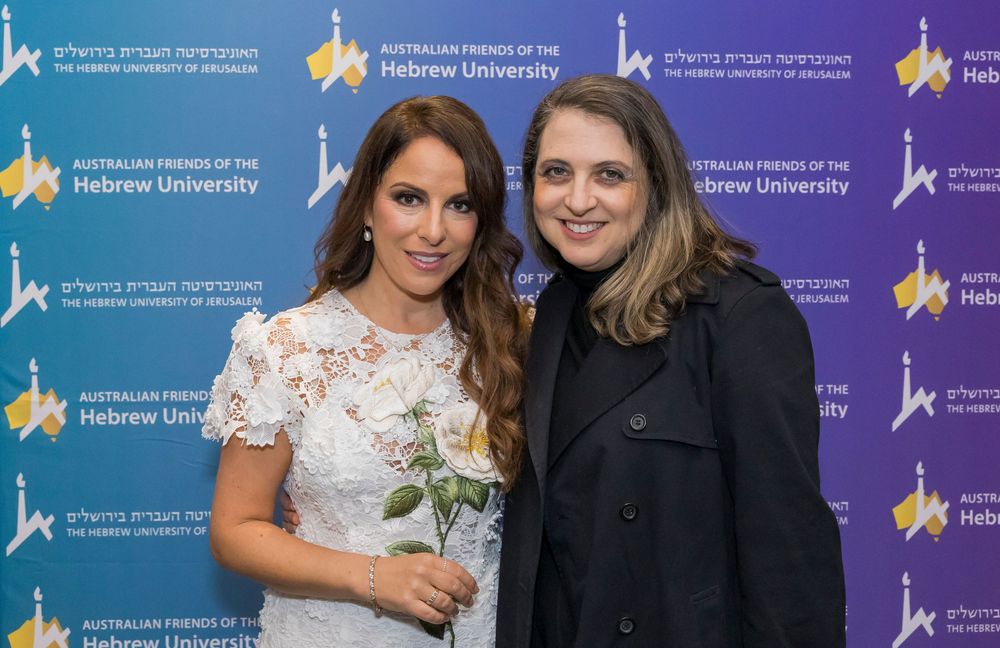 Two attendees pose together at a Hebrew University event with the branded backdrop visible behind them.