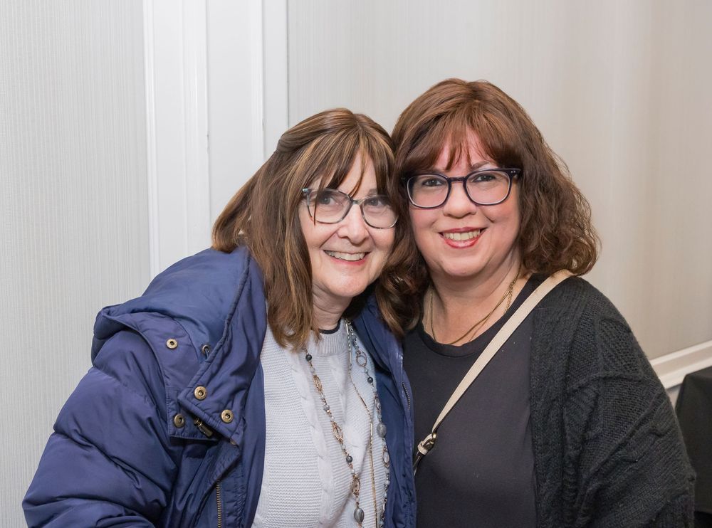 Two people wearing glasses embrace and smile warmly while posing together for the camera.