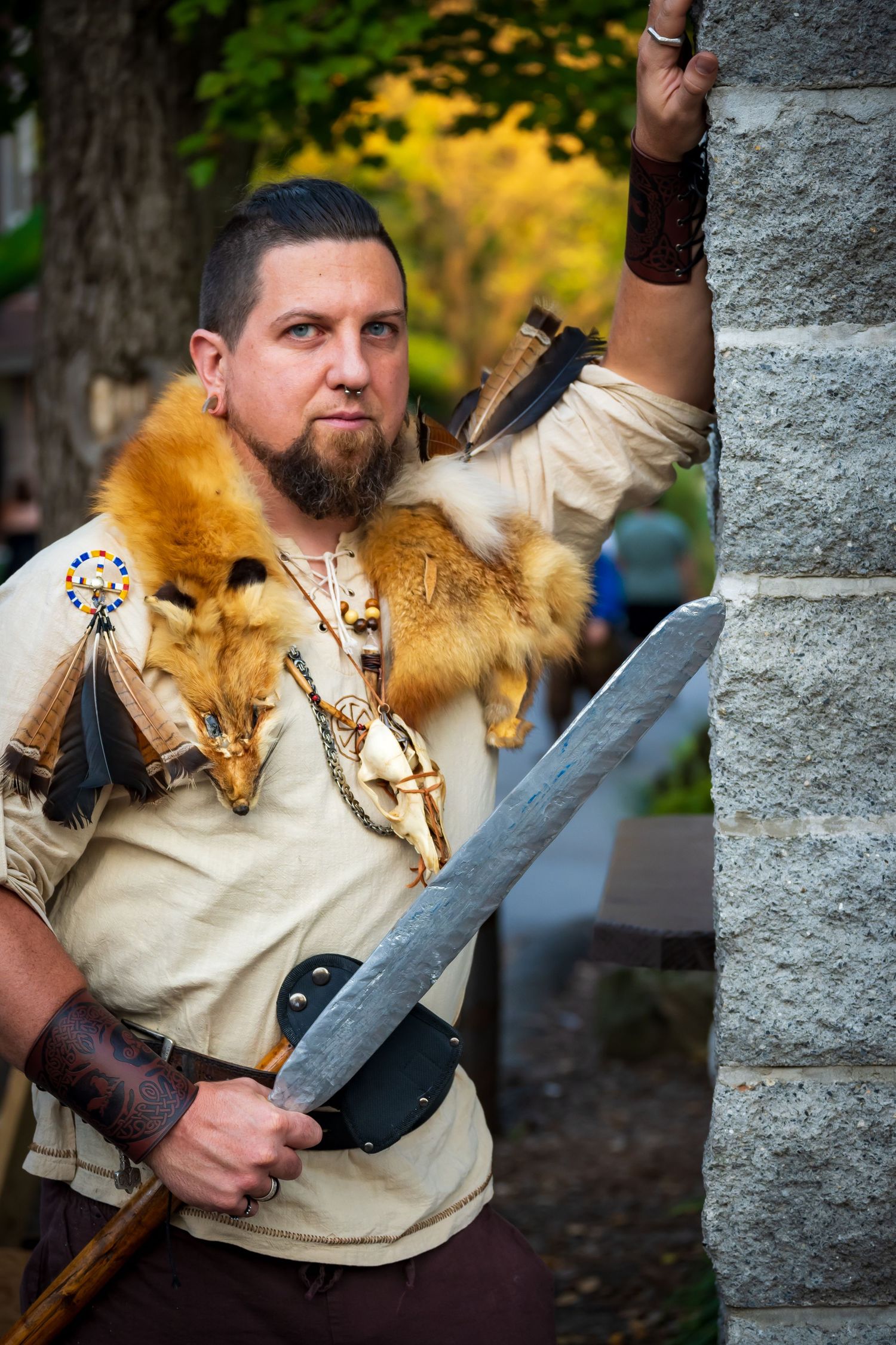 A person in medieval costume with fur and leather garments holds a large sword.
