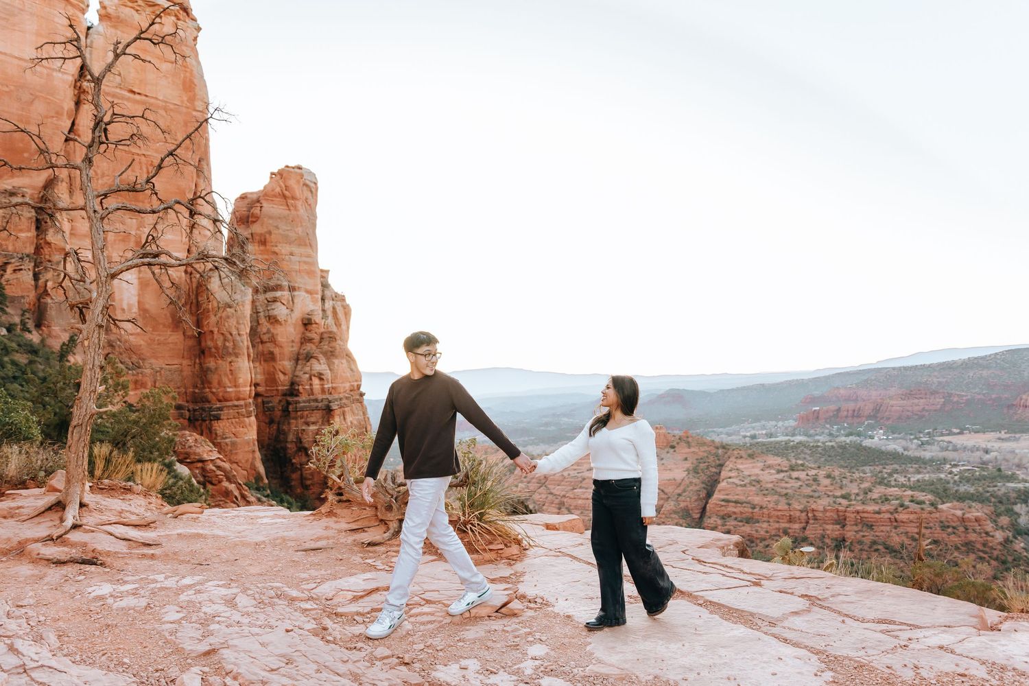 A couple dances playfully on a scenic desert overlook surrounded by red rock formations.