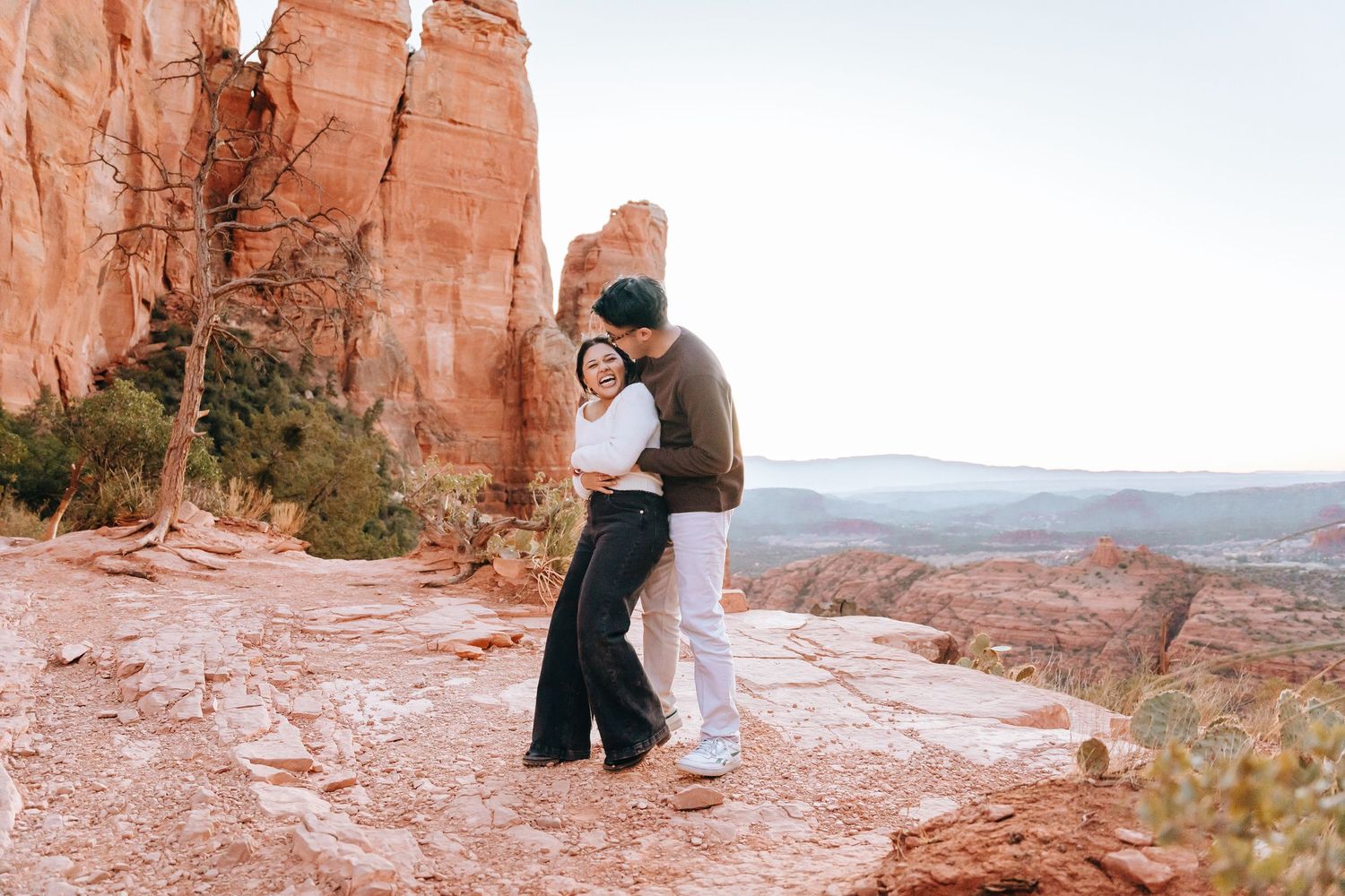 Two people embracing on a scenic overlook with dramatic desert cliffs in the background.