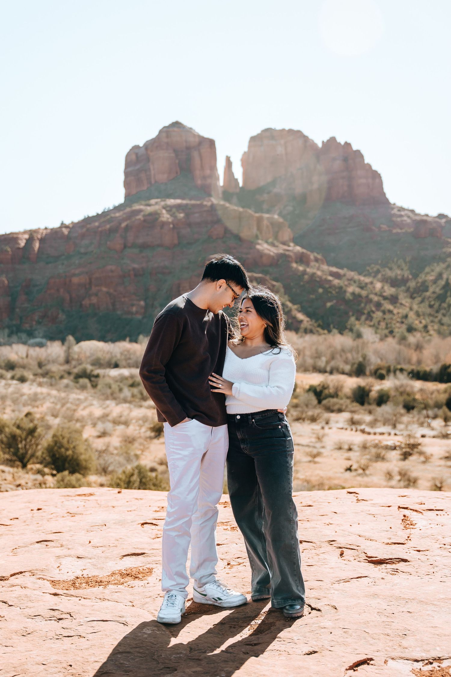 A romantic moment captured on red rocks with Sedona's iconic rock formations in the distance.