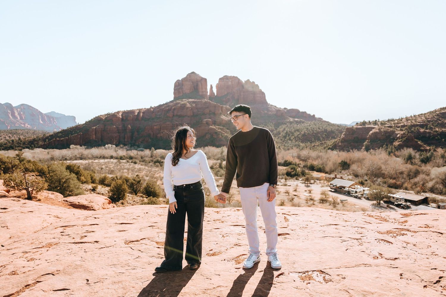 Two people walking hand in hand across red desert rocks with mountains in the distance.