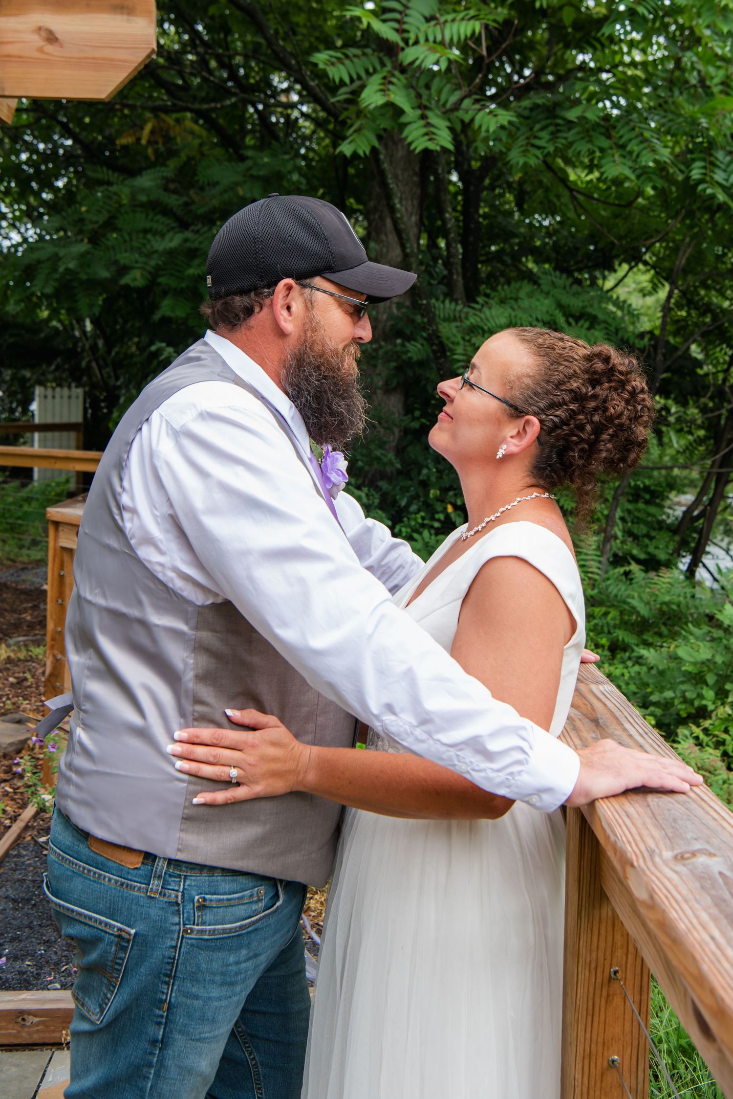 A couple shares an intimate moment on a wooden deck surrounded by lush green foliage on their wedding day.