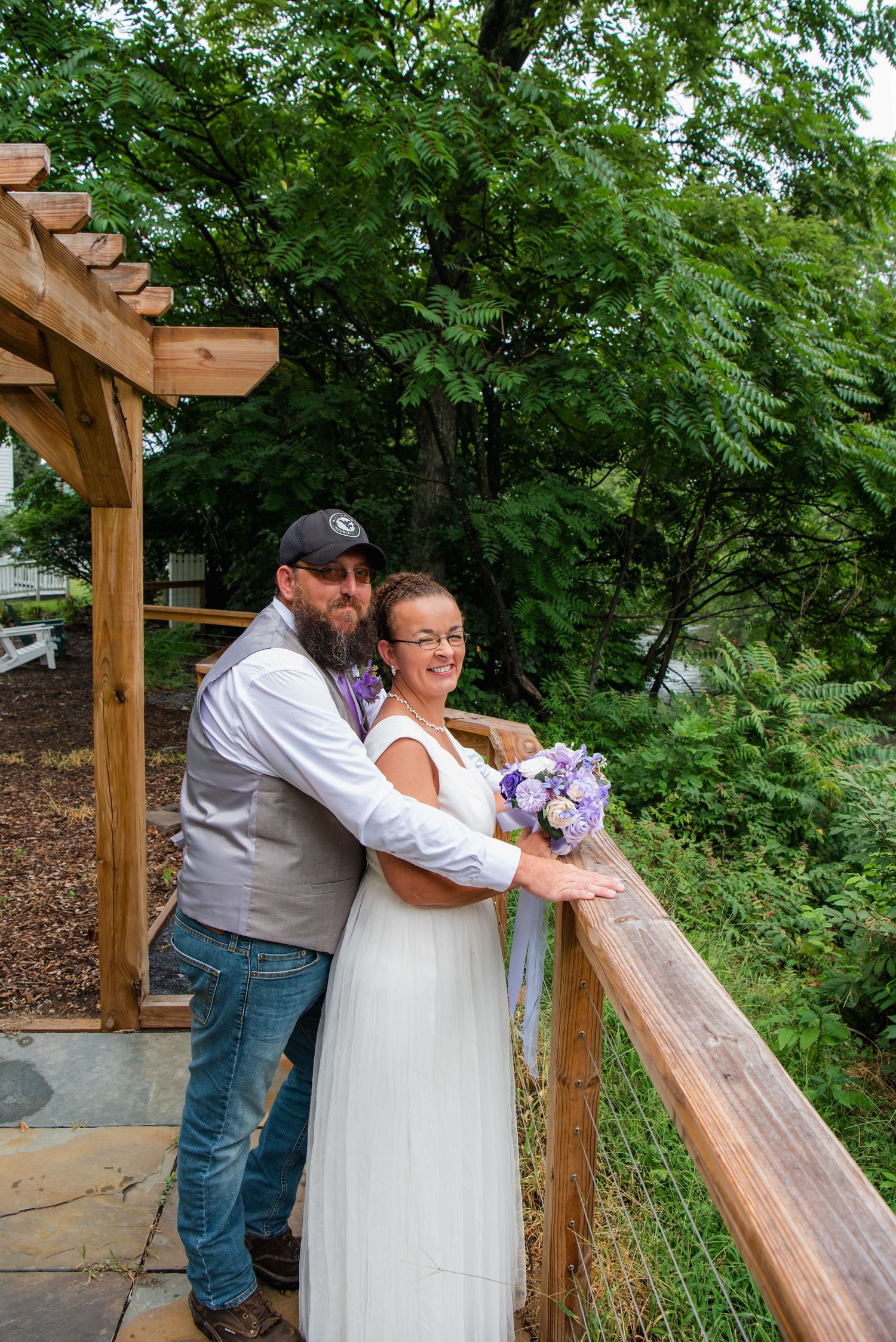 A couple shares a romantic moment under a wooden pergola surrounded by lush greenery during their wedding celebration.