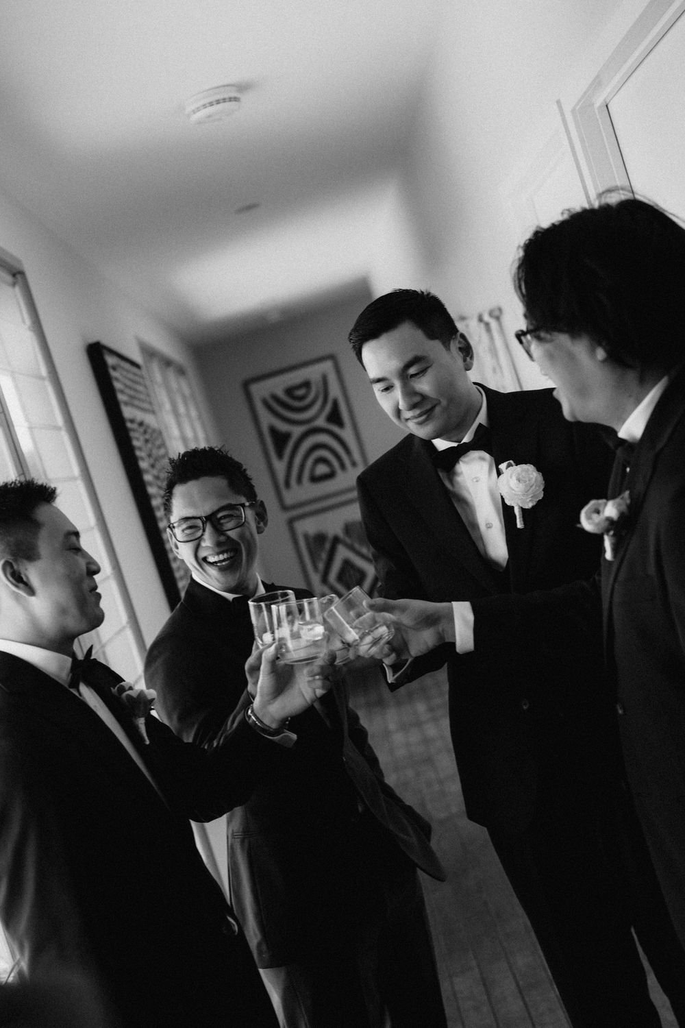 Groomsmen sharing drinks and toasting in formal attire during wedding preparations.