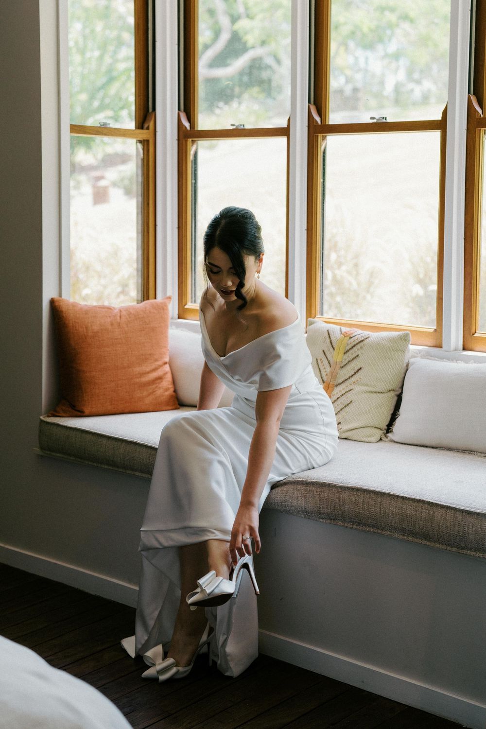 White window seat with orange cushions and white pillows in sequence of getting ready shots.