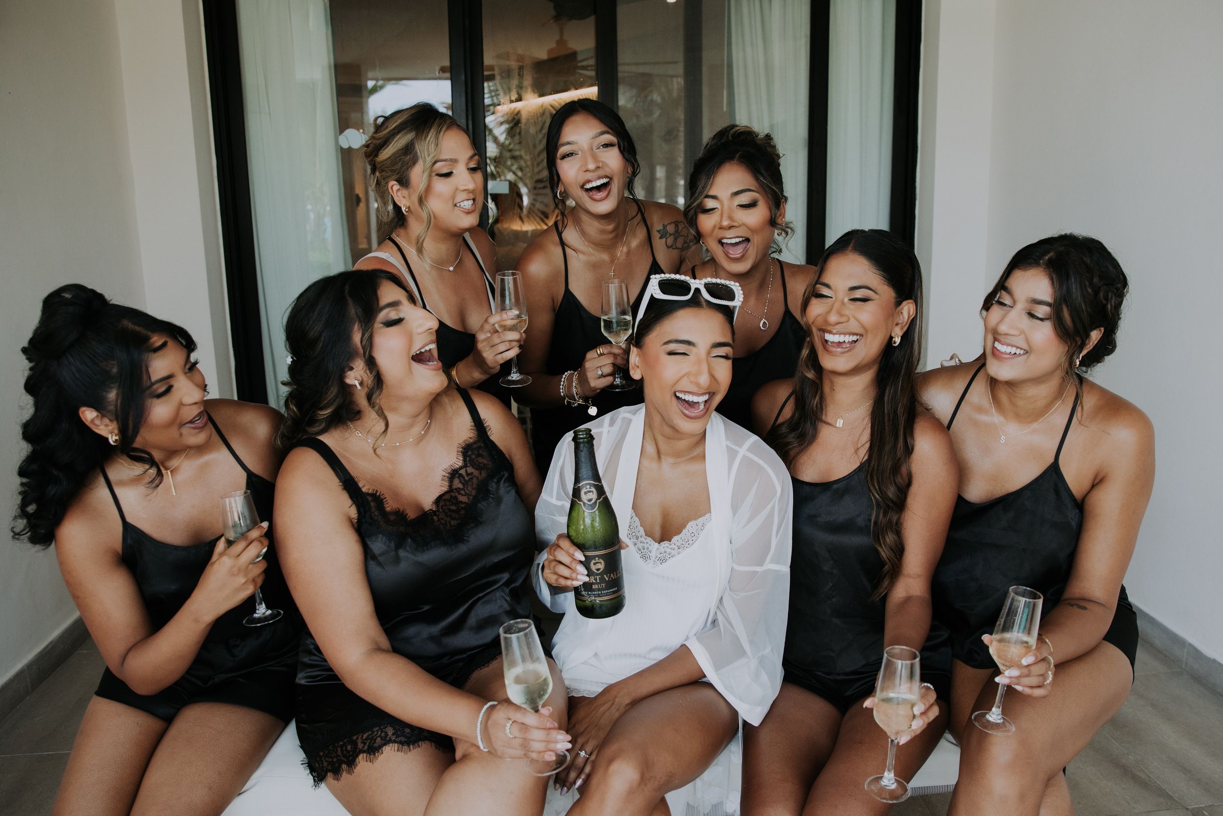 Wedding party celebrates with champagne while wearing dark dresses during pre-ceremony festivities.