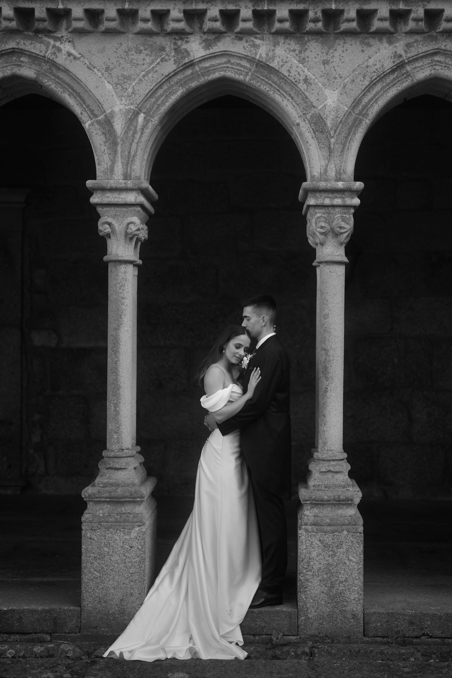 A romantic black and white wedding photo of a couple embracing under ornate stone archways of a historic building.Best wedding photographer