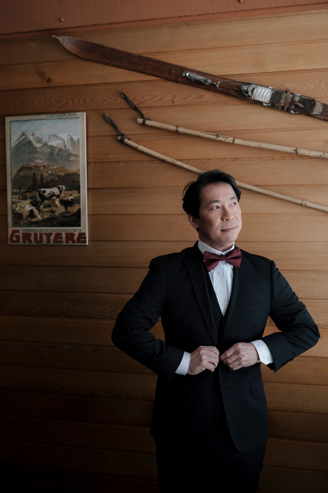 A sequence showing a person in a black tuxedo and bowtie adjusting their attire against a wooden wall backdrop.