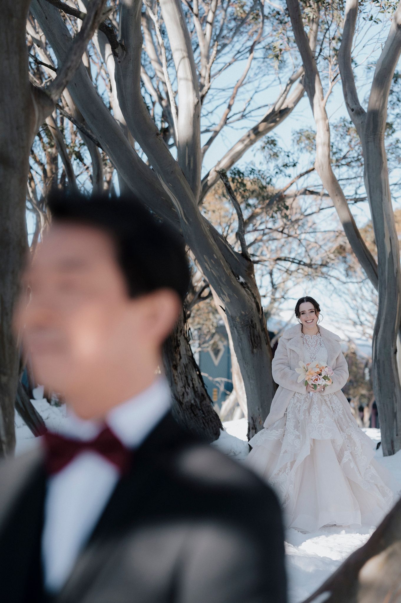 A winter wedding photo taken in a snow-covered forest with ethereal white trees framing people in formal attire.