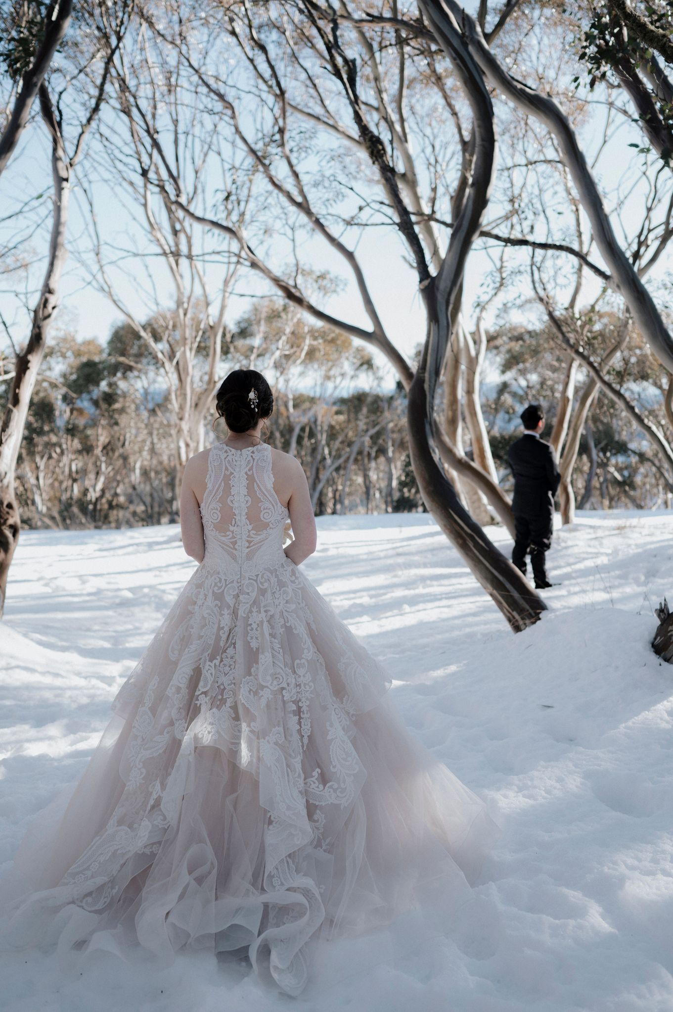 A winter wedding scene with a lace dress in the snow-covered landscape with bare trees in the background.