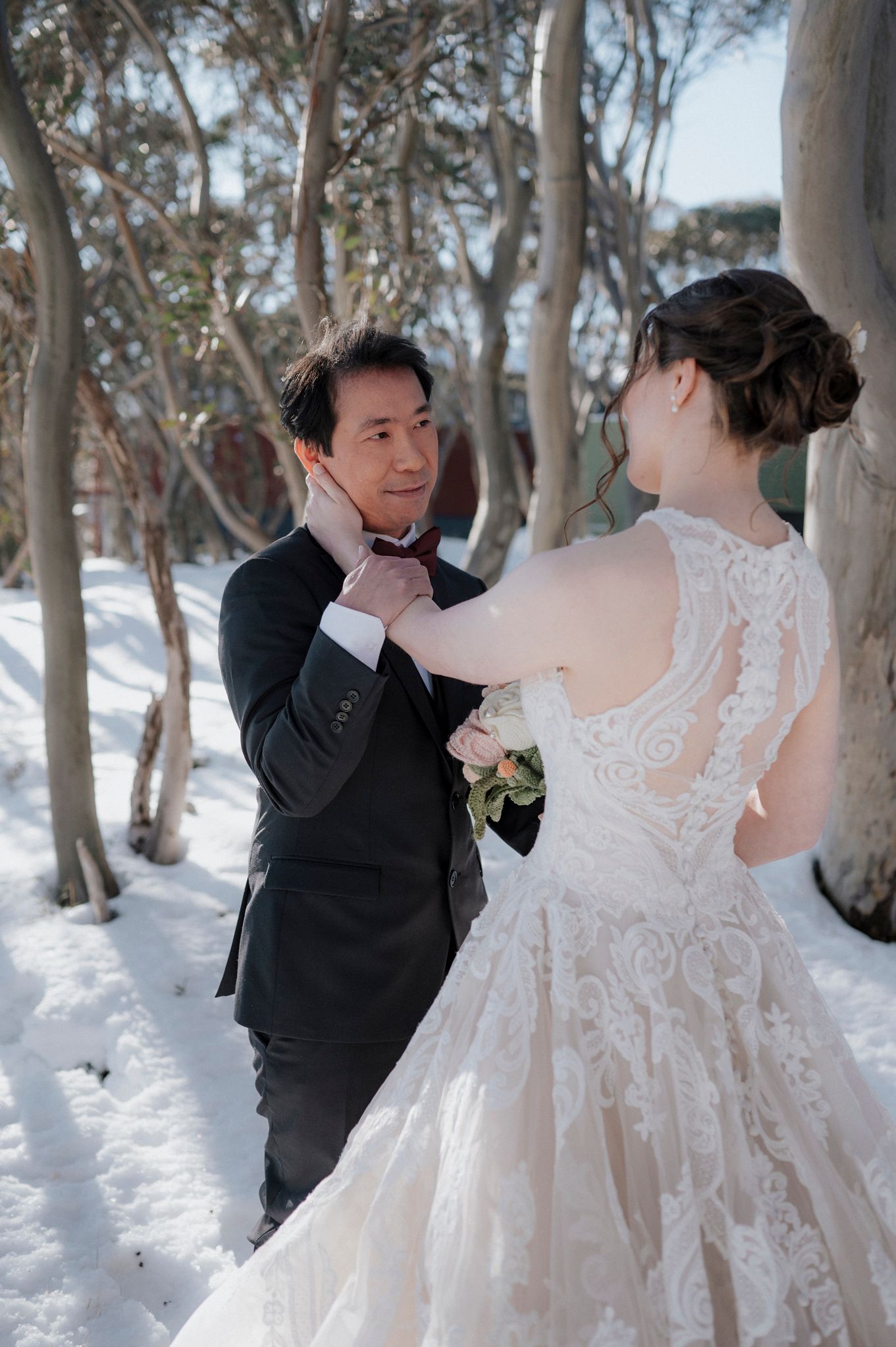 A romantic winter wedding scene showing a couple in formal attire sharing a tender moment among snow-covered trees.