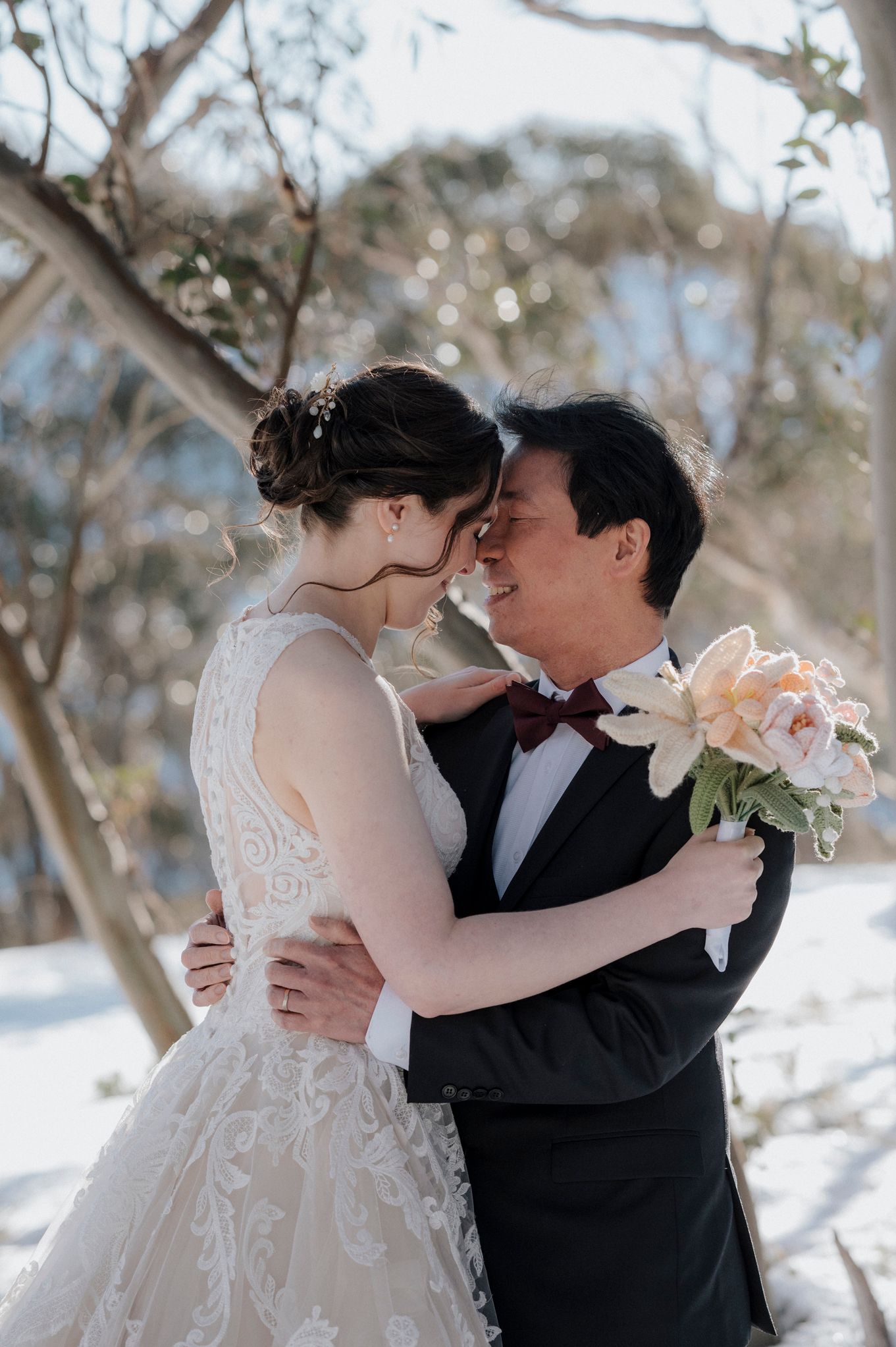 A romantic wedding moment in a snowy winter forest setting with a bouquet of peach-colored flowers.