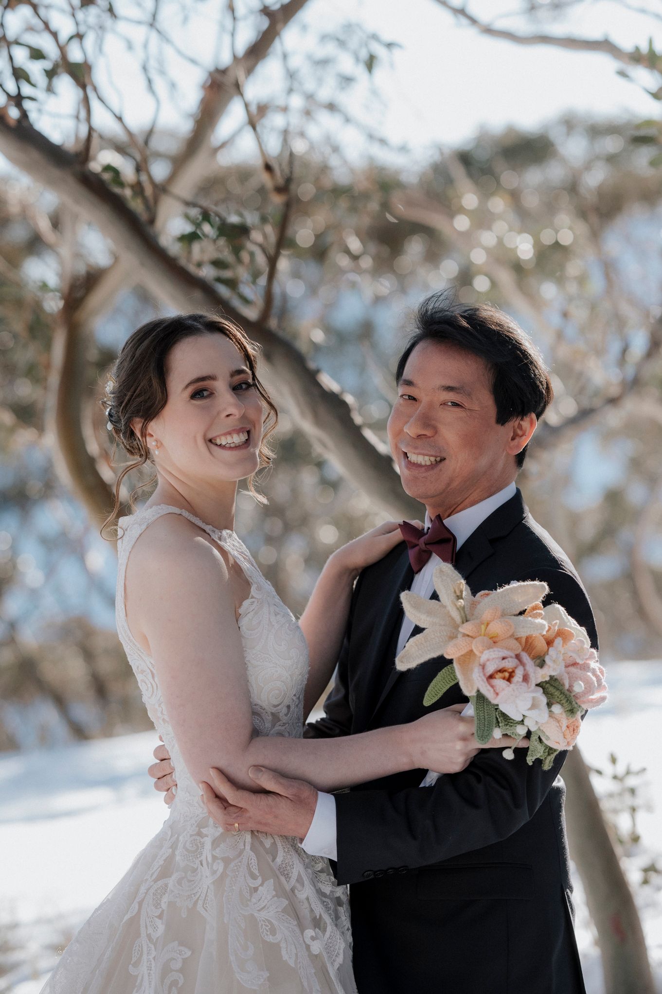 A happy couple share candid moments and laughter together in a snowy winter wedding scene with blooming trees.