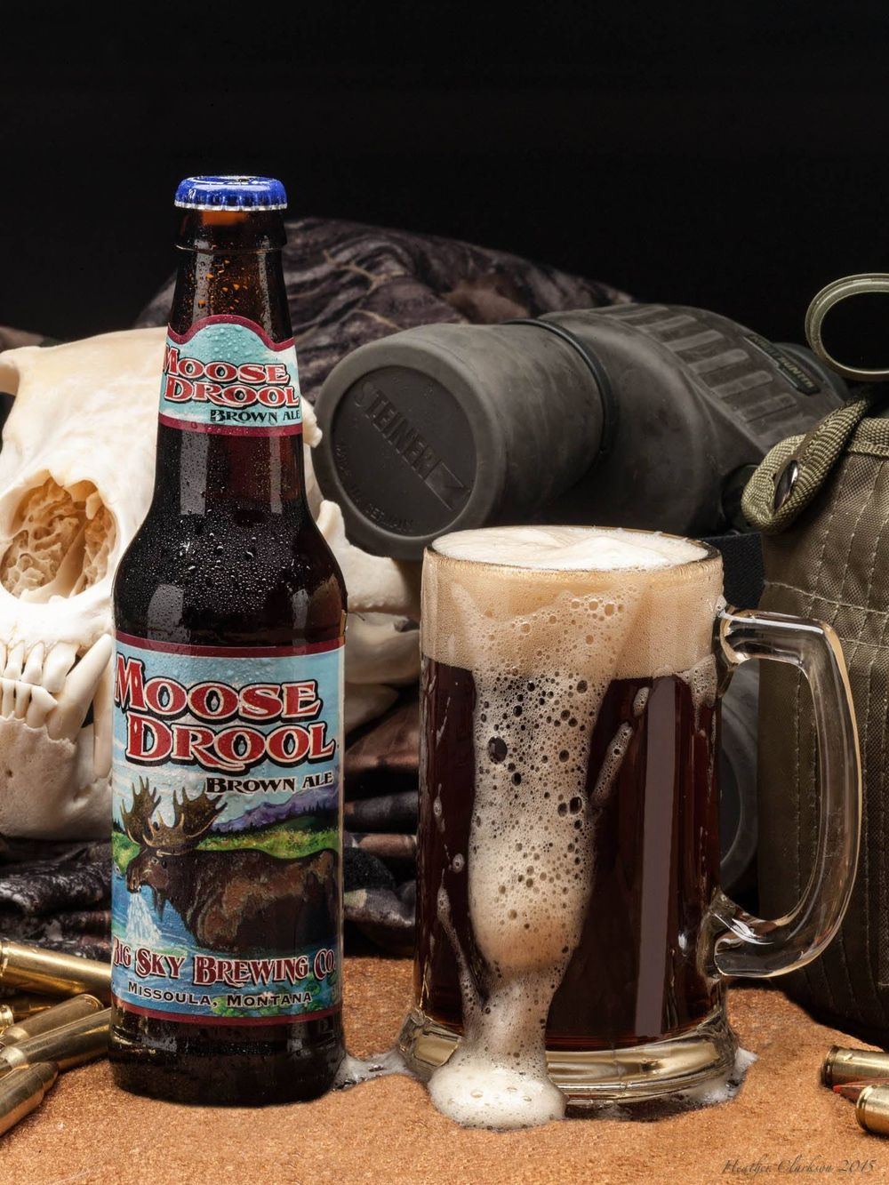 Moose Drool beer bottles and frosty glass mugs with dark beer and foam on a dark background.