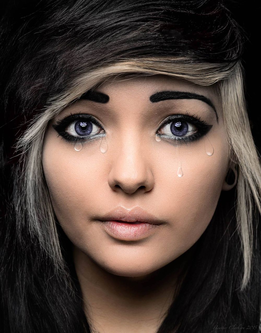 Artistic portrait with dramatic eye makeup and crystal tear details against dark background.
