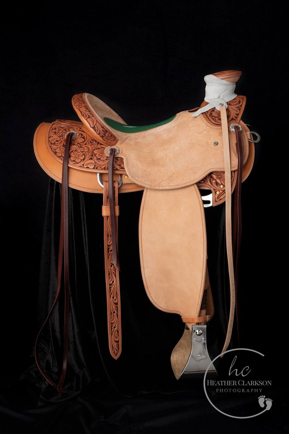 A western leather saddle with ornate tooling and brown leather straps displayed against a black background.