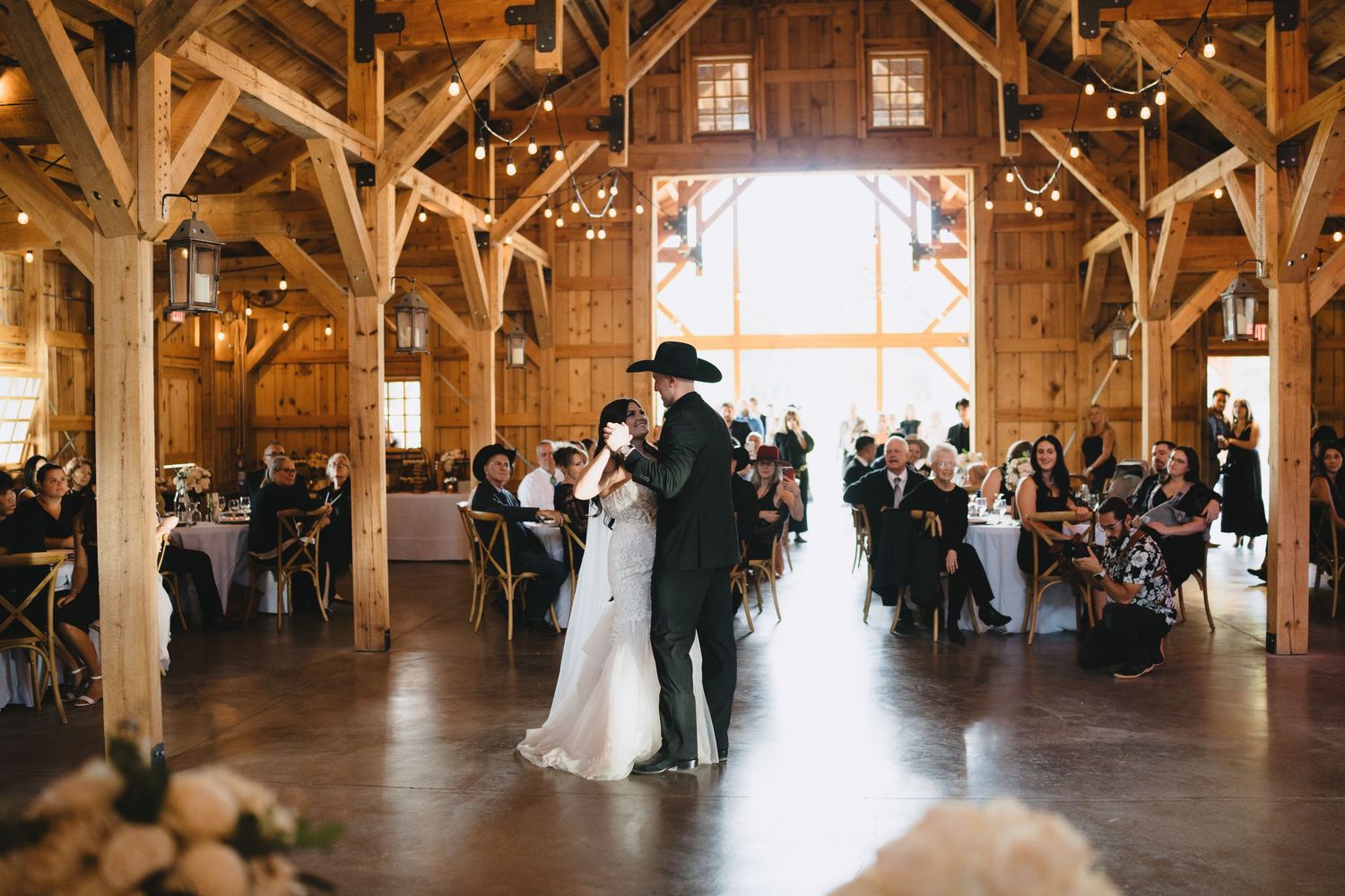 Couple shares first dance in a rustic barn wedding venue with warm string lights and seated guests.Chama Log River Ranch cinematic photograp