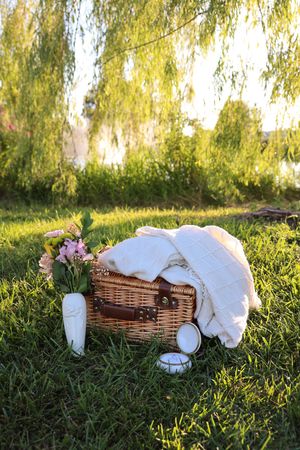 Picnic setup with wicker basket and white fabric on grass under golden willow branches.
