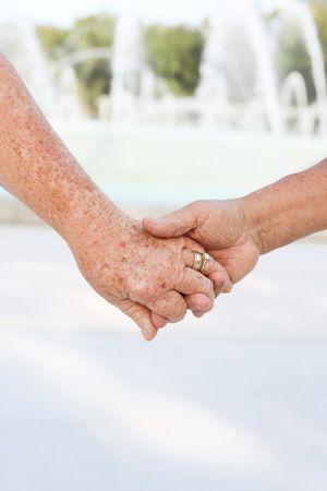 Close-up of hands with wedding rings holding each other against white background.