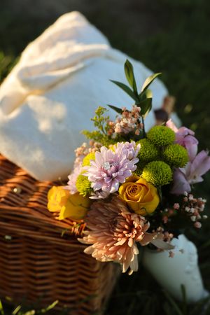 Fresh floral arrangement featuring yellow roses and pink blooms beside a wicker basket at sunset.