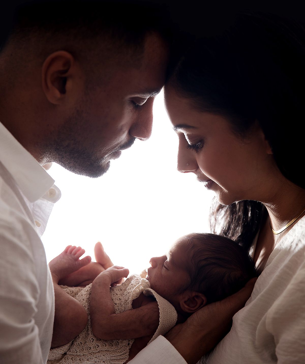An intimate family newborn photoshoot in London. Showing parents holding their newborn baby in soft lighting against a dark background.