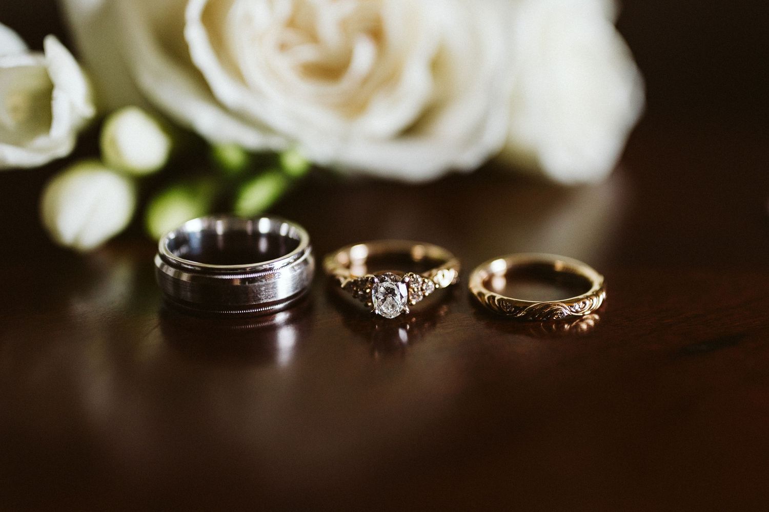 Close-up of wedding rings and white roses on dark background with elegant lighting.