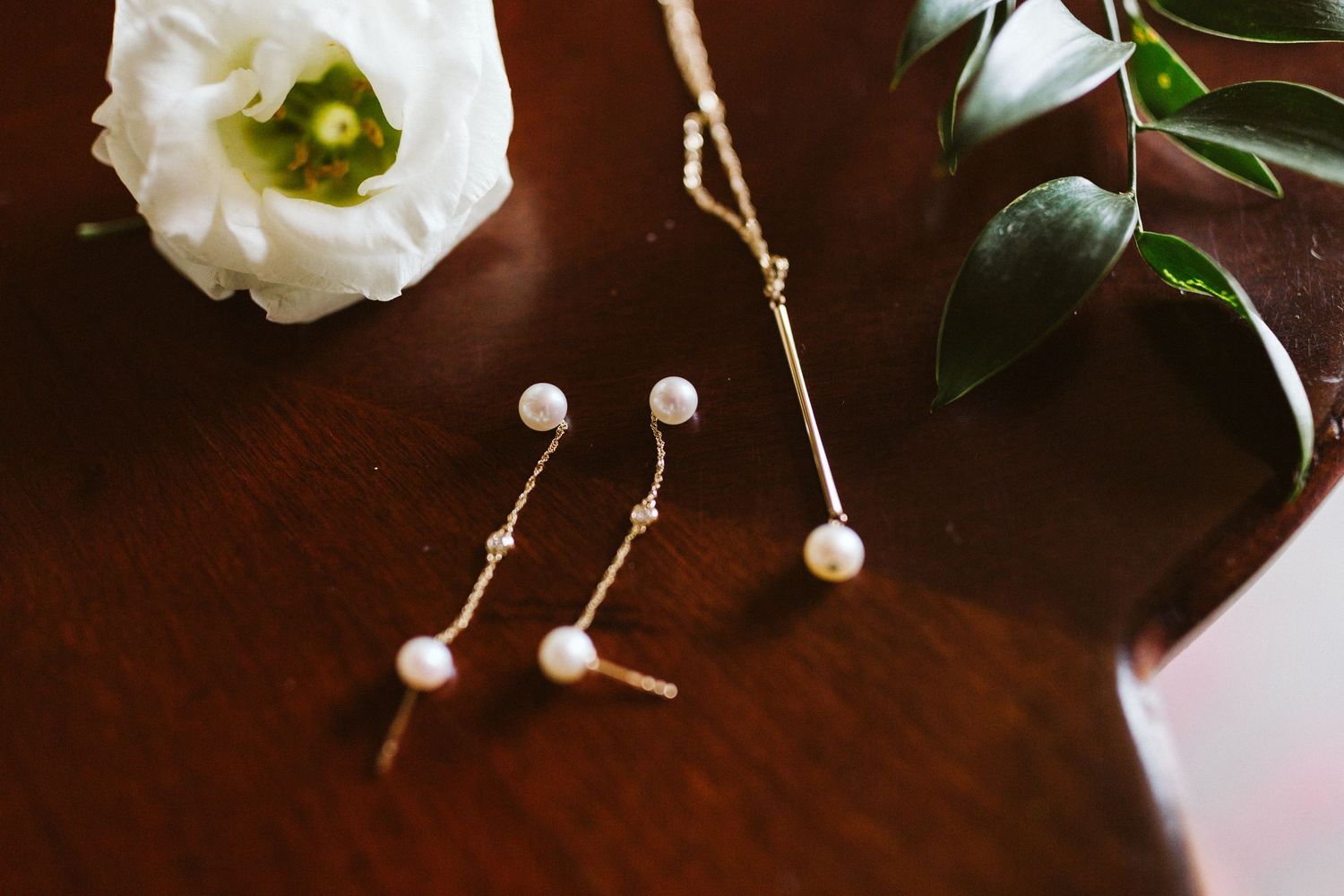 Pearl jewelry and delicate accessories arranged on dark wood surface with floral elements.