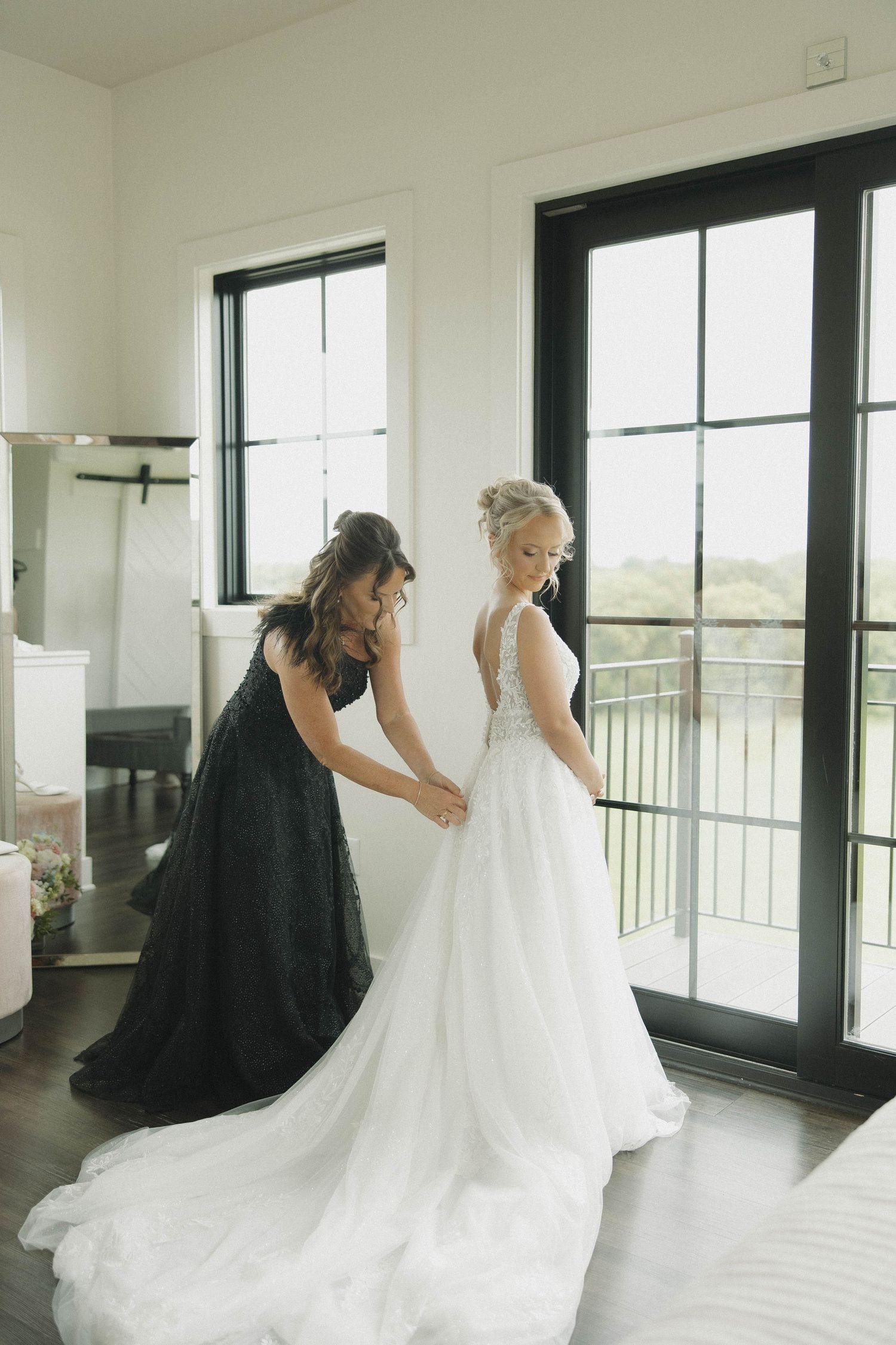 A tender wedding moment captured in a bright indoor space with a bride in white and bridesmaids in black dresses.