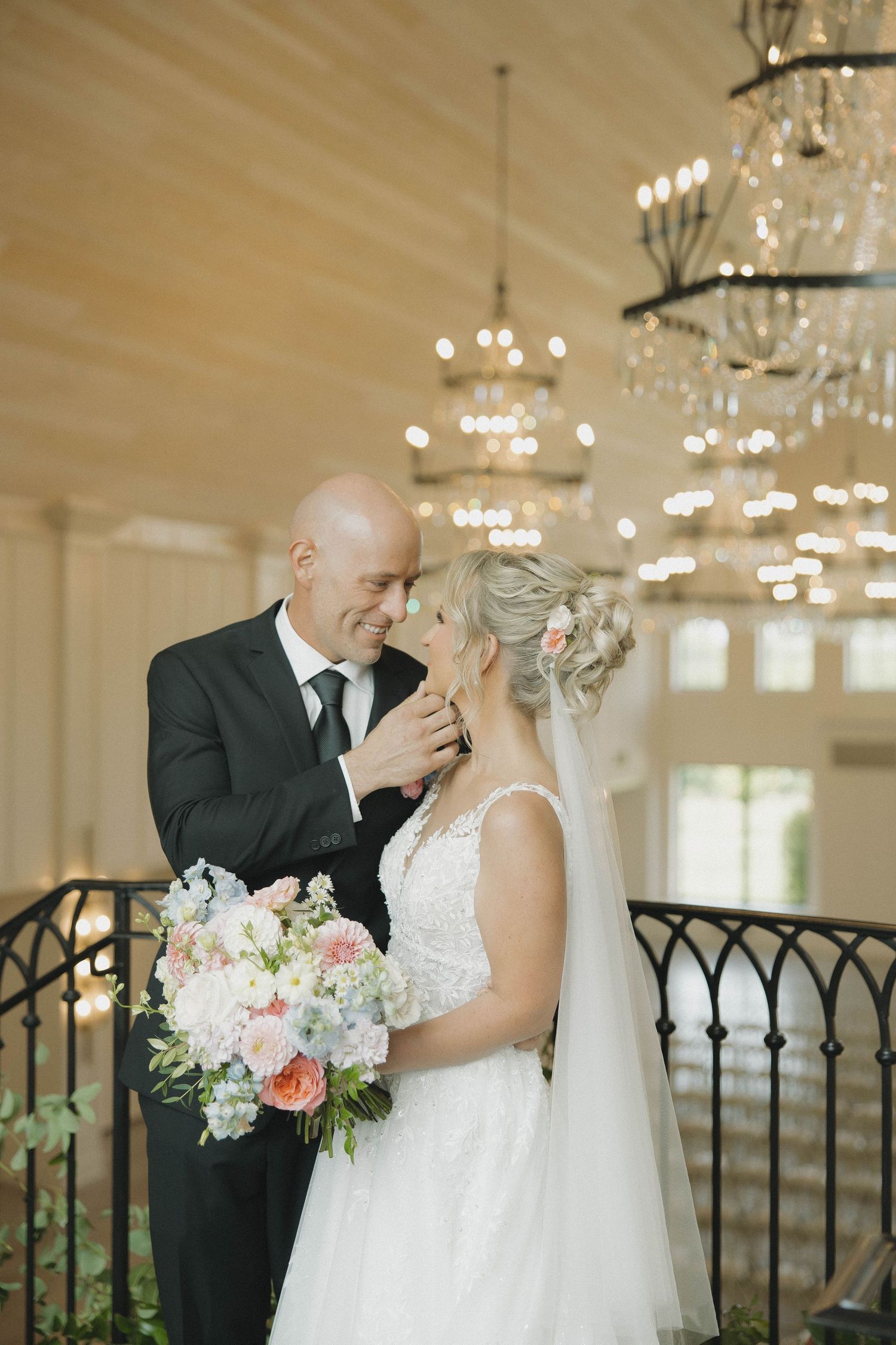 Romantic wedding moment under crystal chandeliers with soft lighting and floral bouquet.
