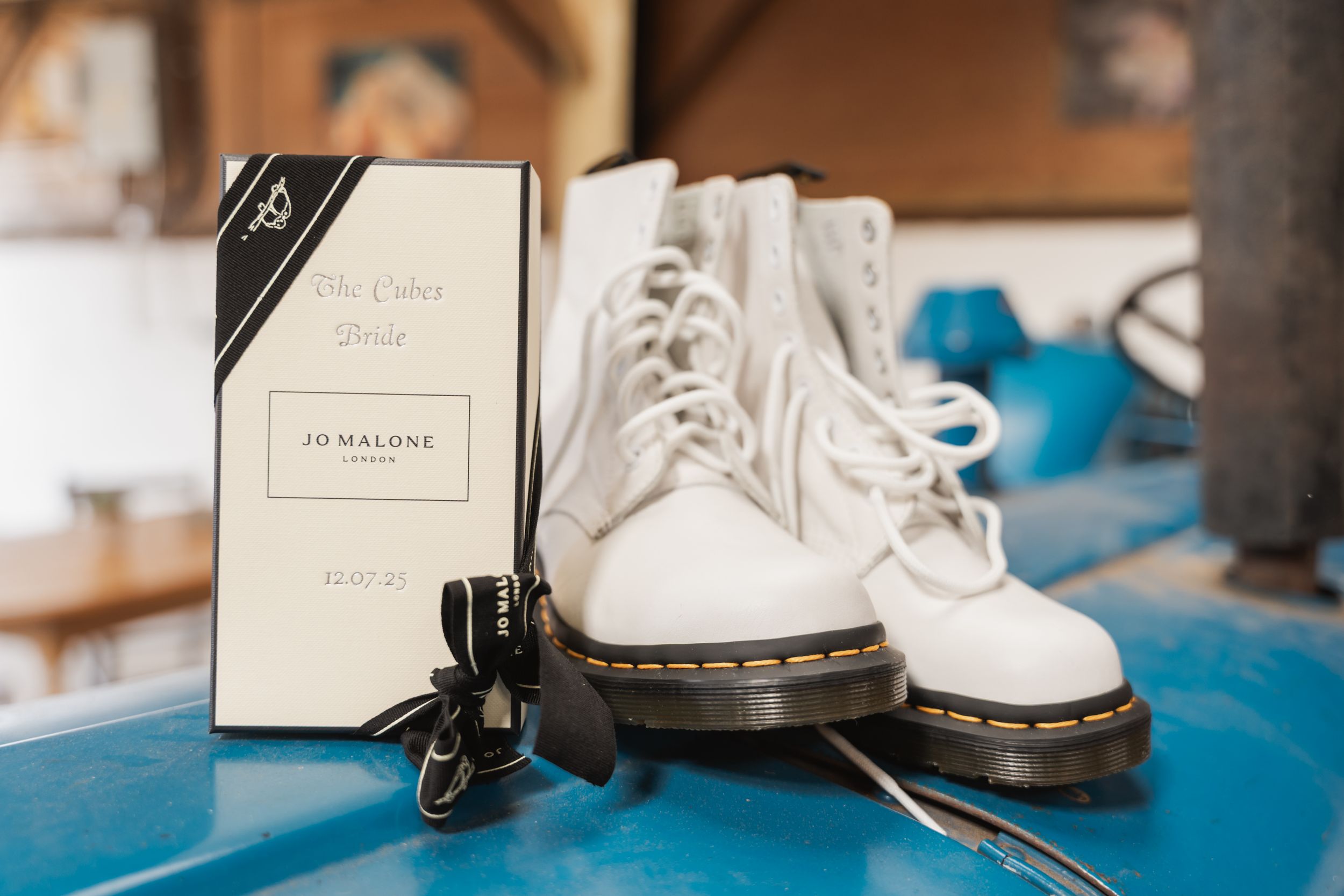White Dr. Martens boots and Jo Malone perfume box displayed on blue surface.