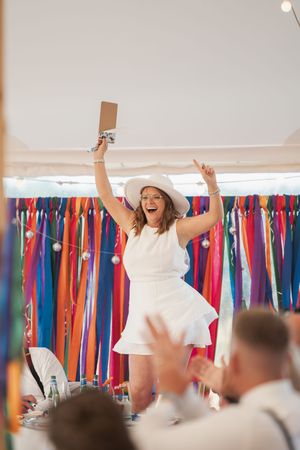 Wedding guests raise their arms in celebration while colorful bridesmaid dresses hang on display racks in the background.