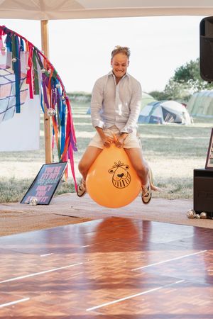 Someone bouncing on an orange space hopper on a wooden dance floor under a tent.