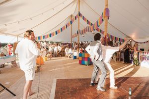 Wedding guests dance enthusiastically under a festive tent decorated with colorful bunting and string lights.