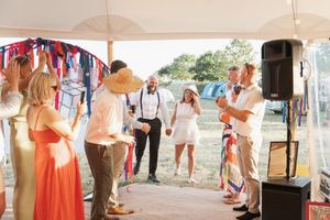 Wedding guests gather under a white tent canopy with red white and blue bunting decorations during a summer celebration.