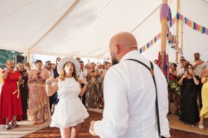 Wedding guests dance and celebrate together under a white tent during a lively outdoor reception.