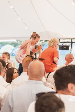 Party guests dancing and celebrating under a white tent with string lights at a festive outdoor event.