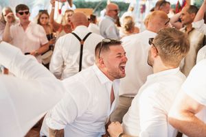 People in white attire celebrating and laughing at an outdoor party event under bright sunlight.