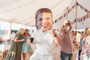 Person wearing white outfit and clear face shield dancing under tent with string lights and colorful banners.