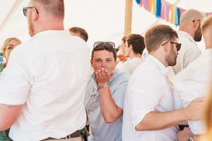 People in white shirts and summer attire mingle at a casual outdoor gathering under a tent.