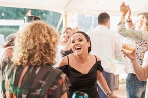 People dancing and having fun at a lively party under a white tent with festive lighting.