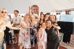 Crowd of party guests dancing and celebrating joyfully under a white tent at a summer event.