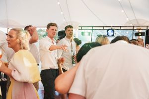 Party guests mingle and dance beneath string lights in a festive tent setting.