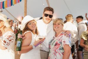 A festive outdoor party scene under a tent with guests enjoying drinks and socializing.