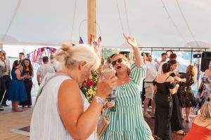 People dancing and celebrating under a white tent at a summer party with festive energy.