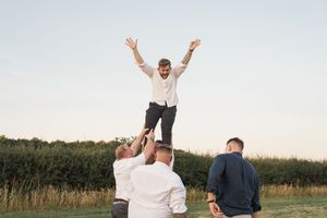 Group having fun outdoors lifting someone up in celebration at sunset in a field.