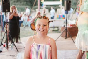 Joyful wedding party attendees wearing colorful summer dresses smile and celebrate at outdoor reception.